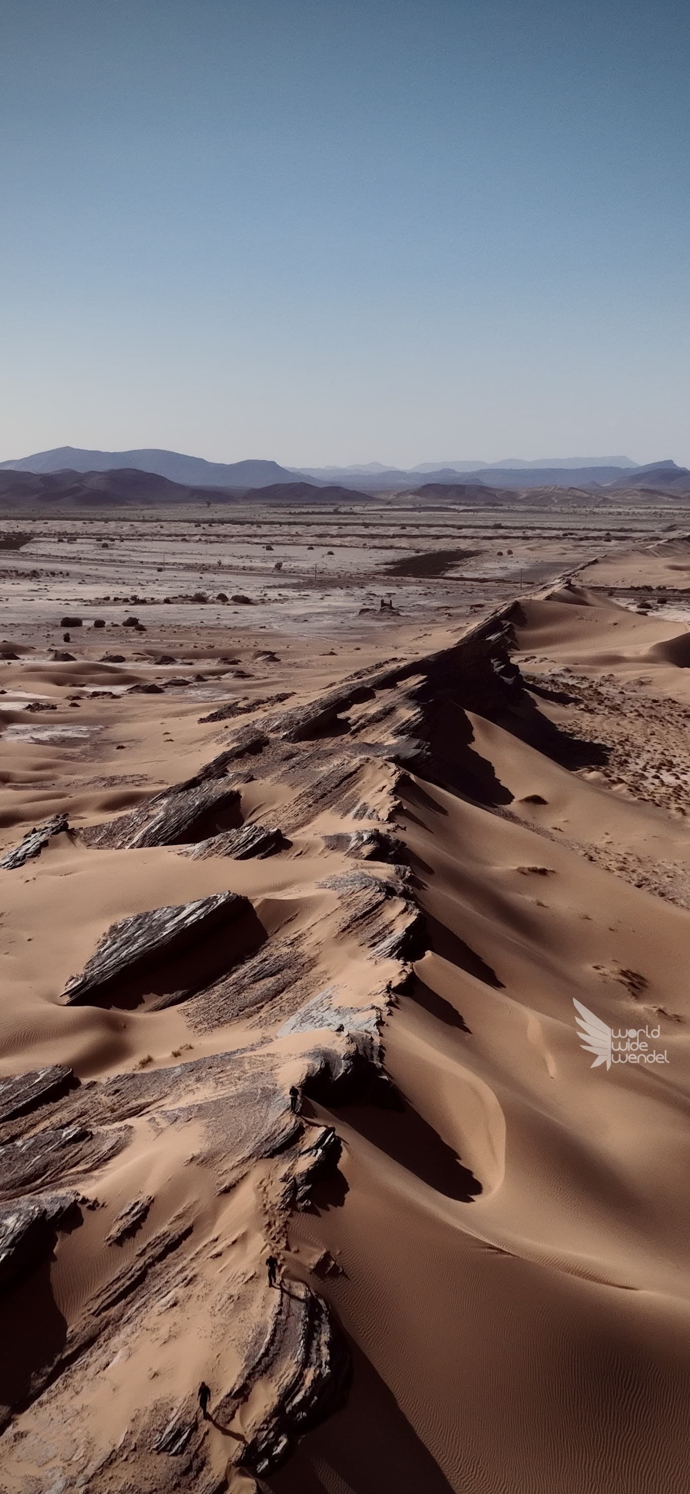 Luchtfoto van een rotsrichel tussen zandduinen met bergen op de achtergrond