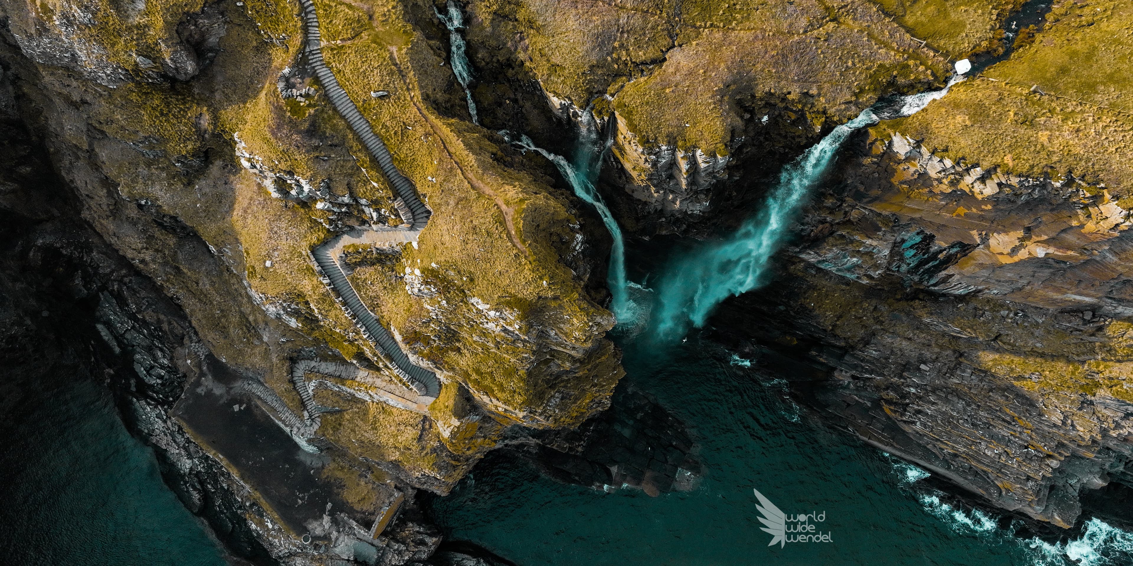 Luchtfoto van een turkooise rivier door een ravijn met een trappenpad langs de kust
