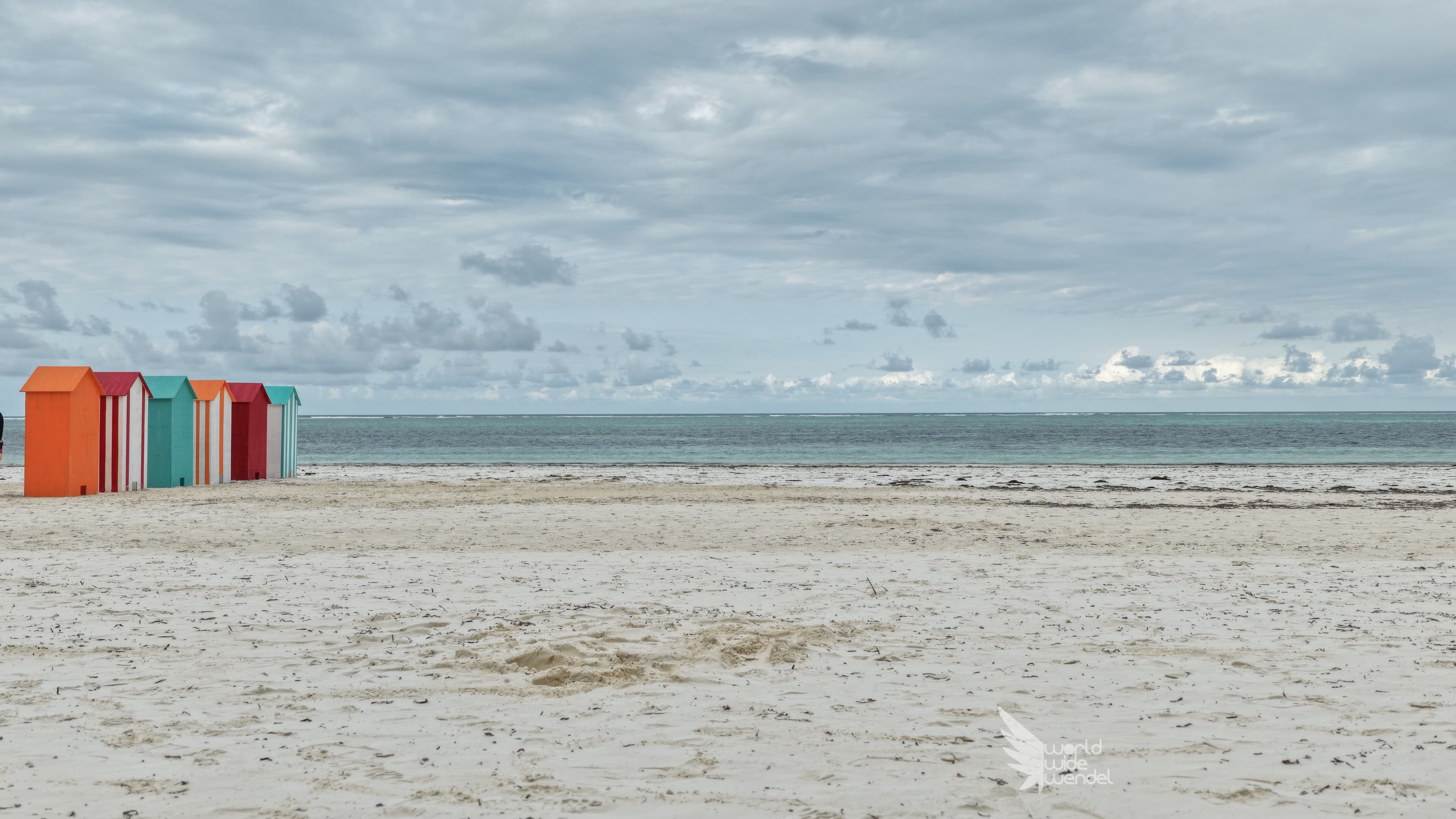 Rij kleurrijke strandhuisjes op een wit zandstrand aan een turkooise zee